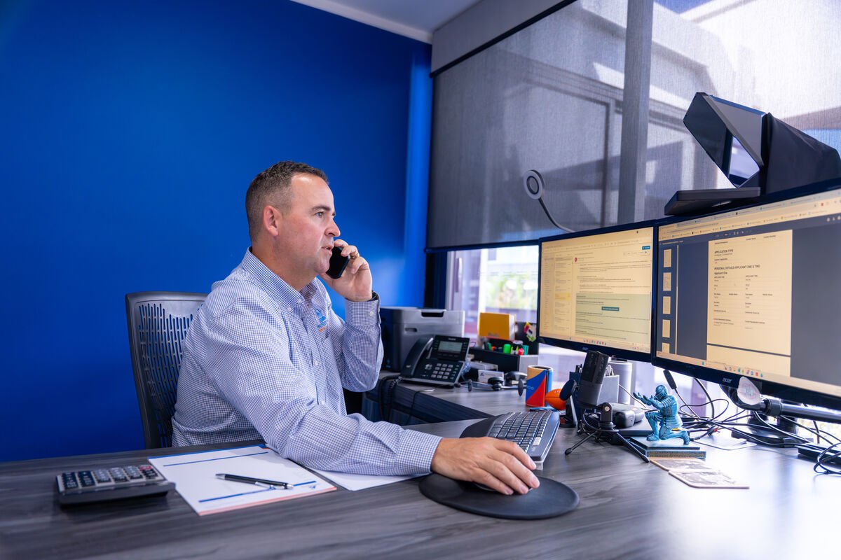 Executive at a corporate desk on a phone call, dual monitors and blue accent wall