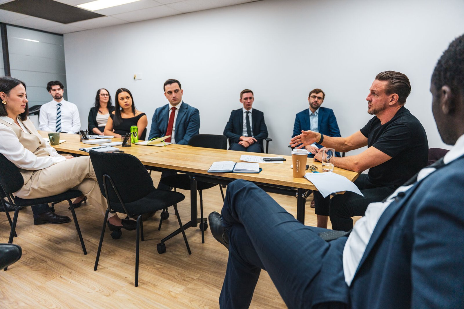 Mid-action panel discussion in a corporate boardroom with the facilitator gesturing across the table